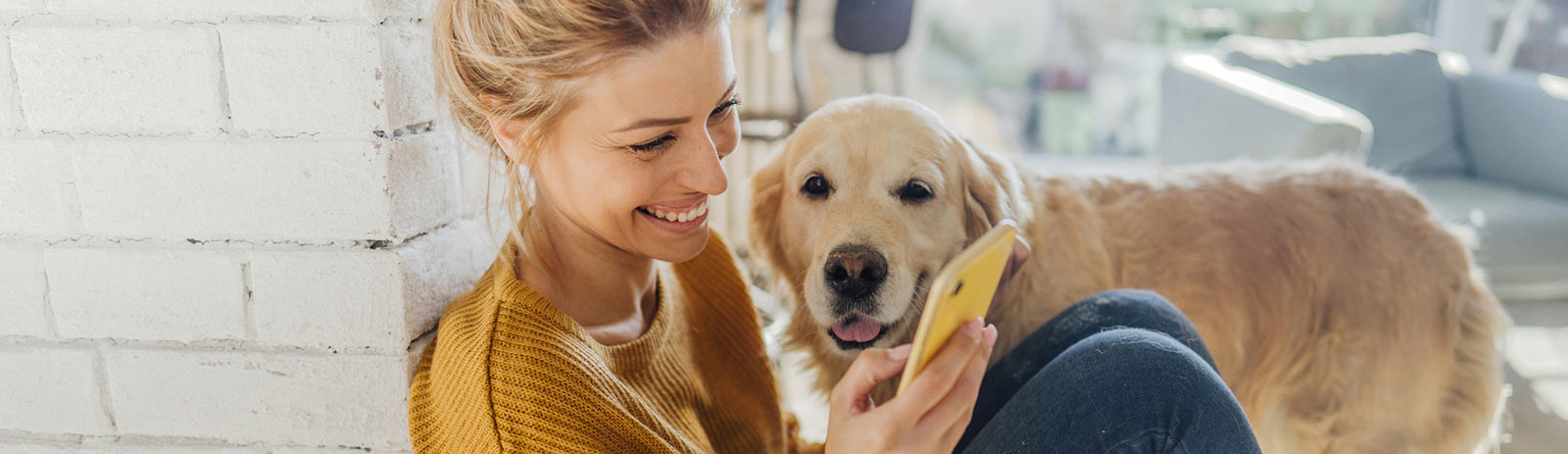 Woman using phone while sitting with her dog in living room